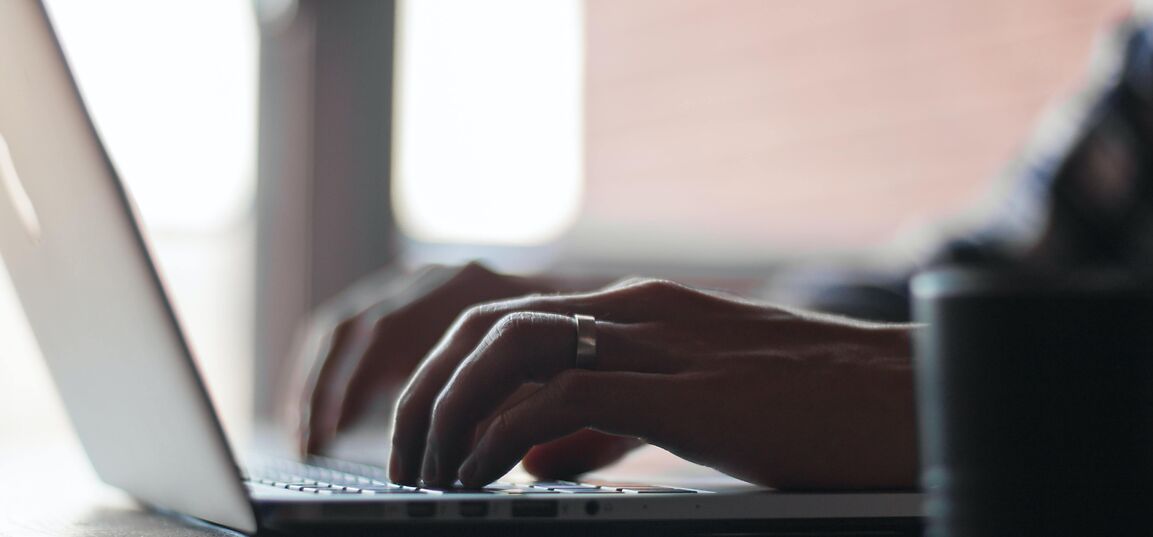 person typing on laptop computer with mug next to them
